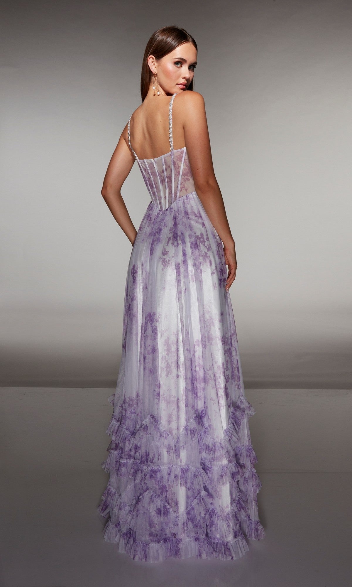 A woman in the Alyce 62202 long prom dress, featuring a sleeveless design, floor length, sheer corset bodice, and lavender floral print, stands facing away and looks over her shoulder.